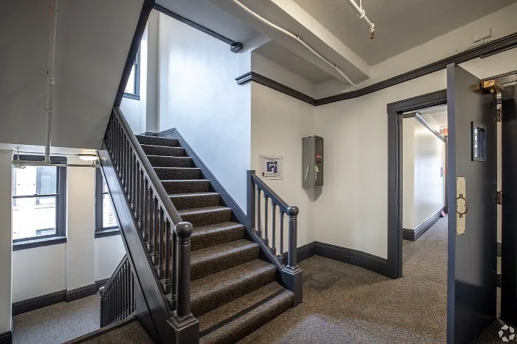 Inviting hallway in modern apartment building featuring elegant staircase with sleek railings and plush carpeting, complemented by large windows for natural light.