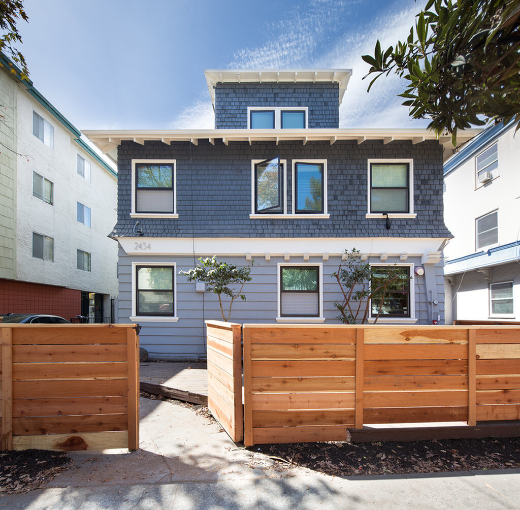 Charming blue townhouse with modern facade and wooden fence, nestled between neighboring buildings.
