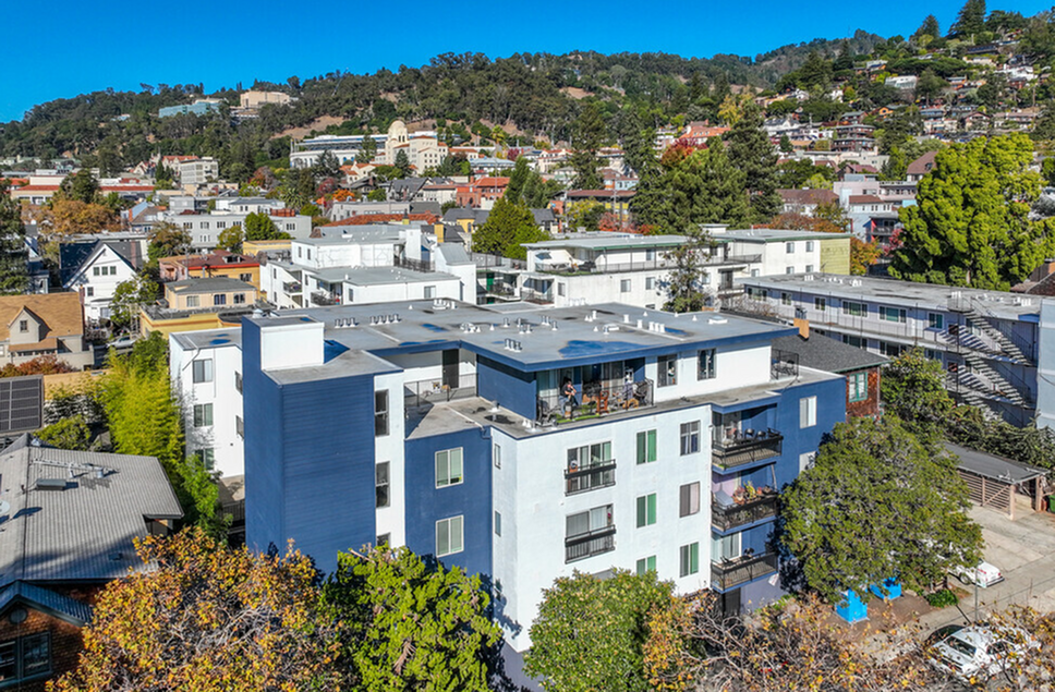 Vibrant neighborhood view with a modern apartment building, scenic hillside backdrop, and lush greenery.