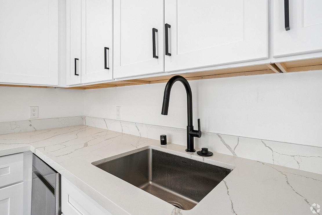 Sleek modern kitchen with elegant marble countertops, stylish black faucet, and pristine white cabinetry.