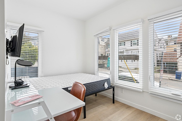 Bright and airy bedroom featuring large windows with blinds, a cozy workspace, and a mounted TV, perfect for comfort and convenience.
