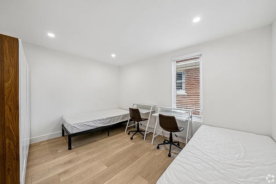 Bright and modern bedroom with two beds, study desks, and sleek hardwood flooring, perfect for a comfortable living experience.