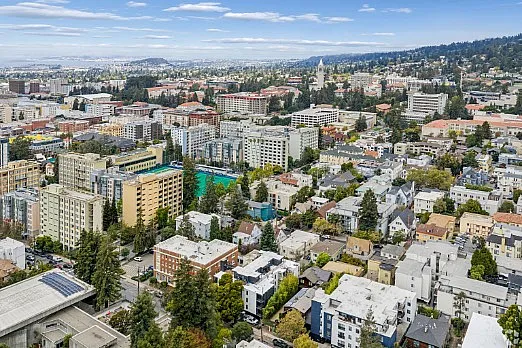 Vibrant aerial view of a bustling cityscape with diverse architecture, lush greenery, and a backdrop of rolling hills and blue skies.