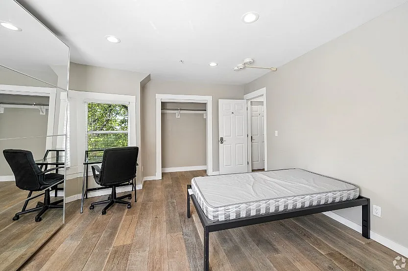 Bright and airy bedroom with sleek wooden flooring, large mirrored closet, and a cozy study nook overlooking green scenery.