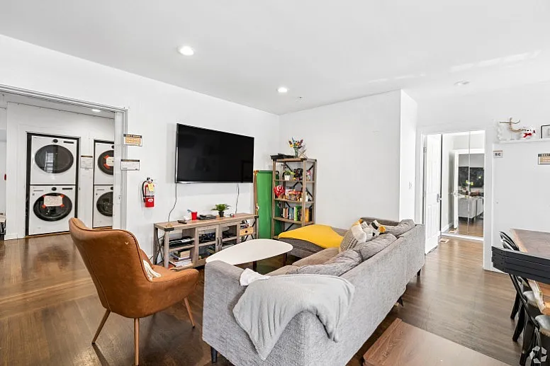 Bright and welcoming living room featuring a cozy sofa, modern TV setup, and an inviting open layout leading to a dining area, perfect for relaxation and entertainment.