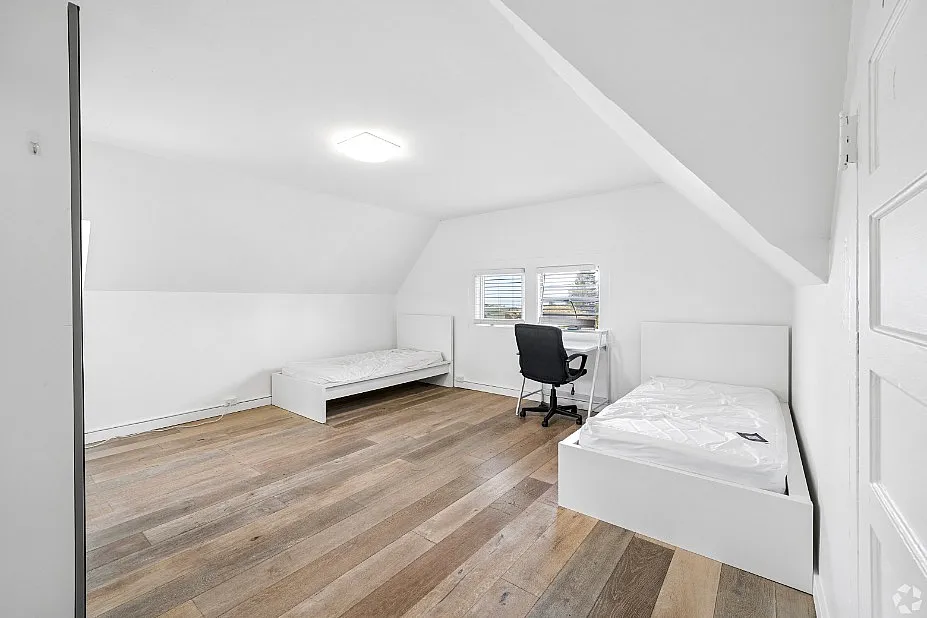Bright and spacious attic bedroom with two single beds, wooden floors, and a cozy workspace by the window.