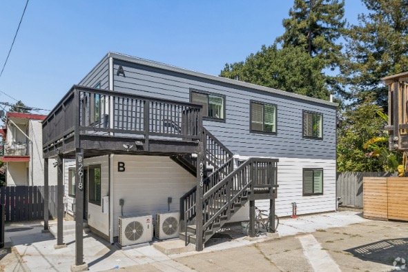 Contemporary two-story duplex with sleek gray siding and private balconies set amidst lush greenery.