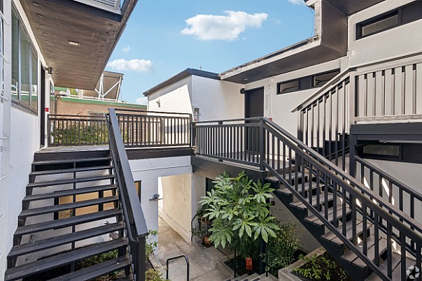 Charming apartment exterior with modern black railings and lush greenery, offering easy access through stylish staircases under a bright blue sky.