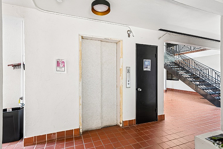 Modern apartment hallway with clean design featuring elevator access and a stylish staircase with sleek railings.