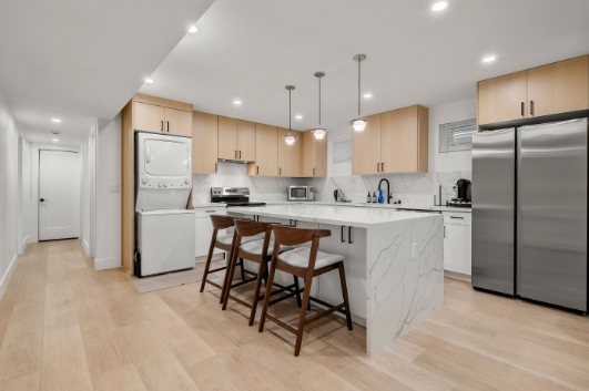 Modern kitchen with sleek marble countertops, integrated appliances, and warm wood cabinetry, featuring an inviting dining area with bar seating.