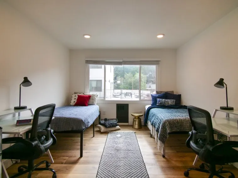 Bright and spacious bedroom featuring twin beds, modern desks, and large window with scenic views.