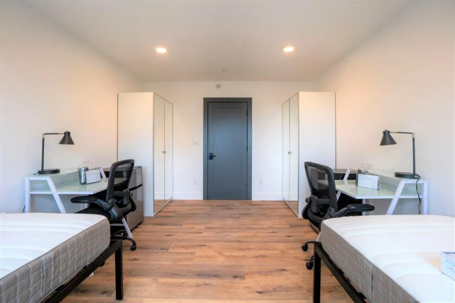 Spacious modern bedroom with twin beds, stylish workstations, and sleek lighting in a bright, minimalist design.