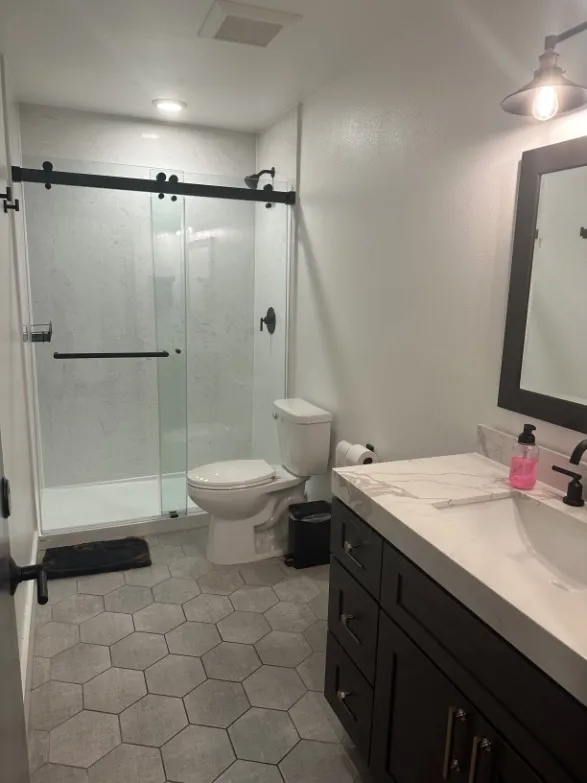 Modern bathroom featuring a sleek glass-enclosed shower, stylish hexagonal floor tiles, and a contemporary vanity with elegant lighting.