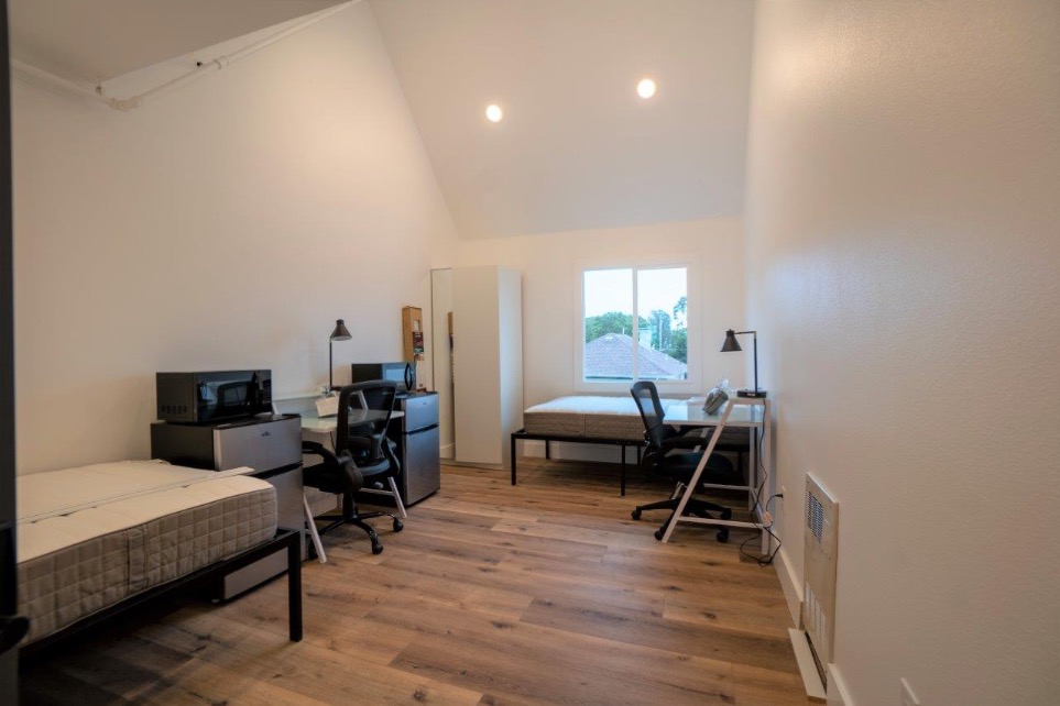 Modern dual-bedroom space featuring sleek desks and comfortable chairs, complemented by natural light and warm wooden flooring.