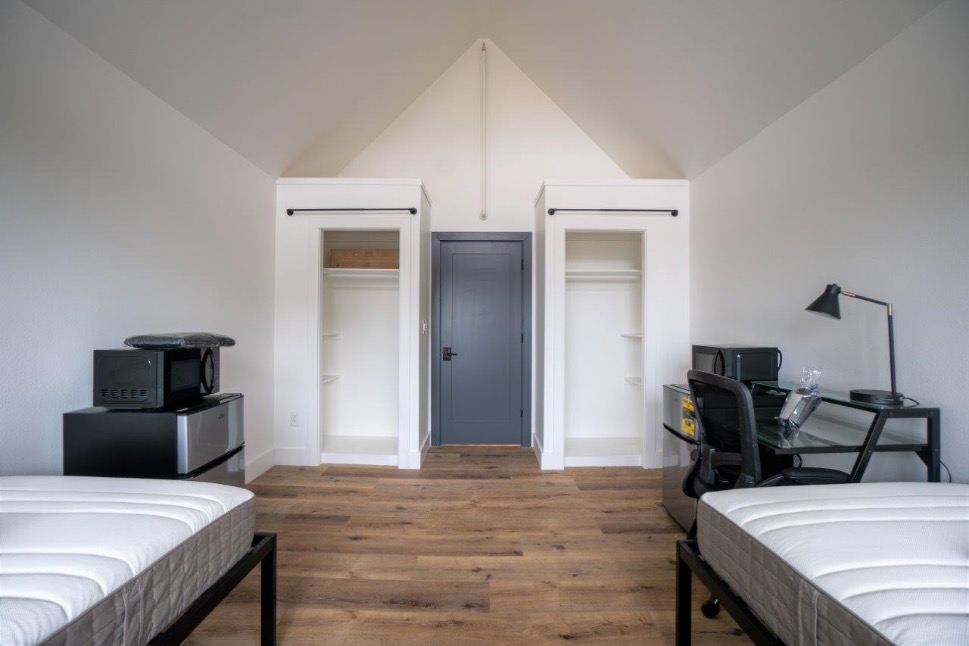 Modern bedroom with high ceiling, featuring twin beds, a sleek workspace, and built-in storage, ideal for comfortable living.