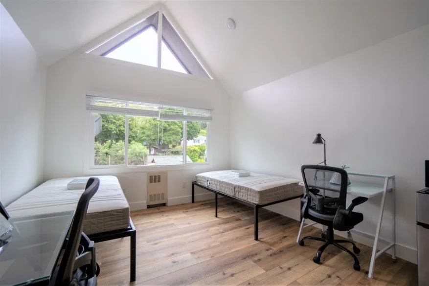 Bright and airy bedroom with vaulted ceiling, featuring two twin beds, a desk, and large window with scenic views.