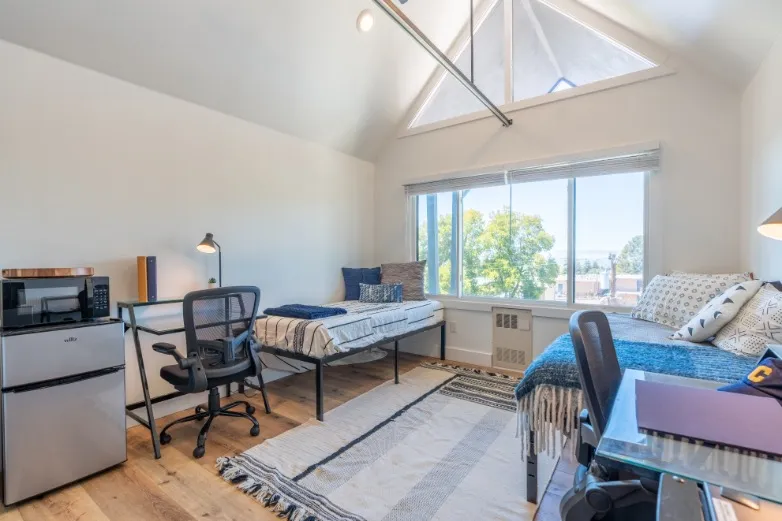 Bright and inviting room featuring two cozy beds, large windows with scenic views, and a stylish workspace, perfect for comfort and productivity.