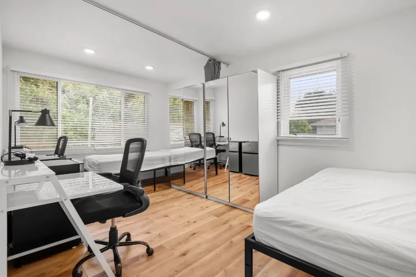 Bright and modern bedroom with large mirrored closet, cozy workspaces, and elegant wood flooring.