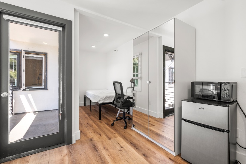 Bright and modern room featuring sleek hardwood floors, a mirrored wardrobe, and access to a private balcony.