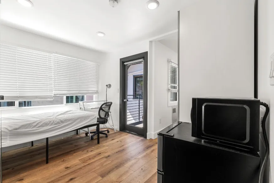 Bright and modern bedroom with sleek hardwood floors, a cozy bed, and a stylish desk, highlighting a private balcony access.