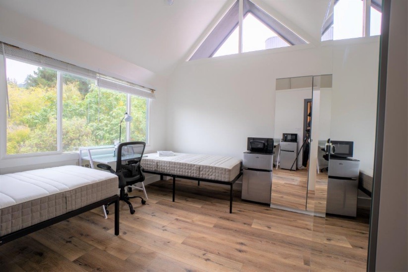 Bright and airy bedroom with two cozy beds, large windows with nature views, and modern amenities including a mini fridge and microwave.