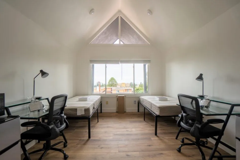 Bright and airy bedroom with vaulted ceiling, two beds, and modern desks, featuring large window with scenic view.