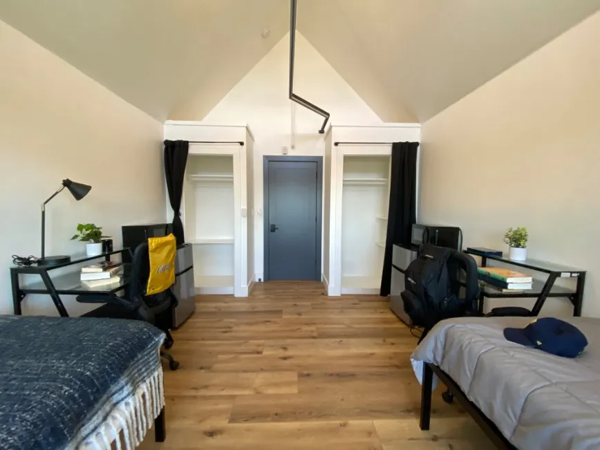 Bright and modern bedroom space with vaulted ceiling, featuring two workspace desks, cozy beds, and spacious closets, ideal for comfortable student living.