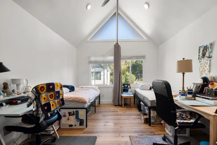 Bright and inviting bedroom with two cozy beds, vaulted ceiling, and a large window offering a pleasant outdoor view, perfect for a shared living experience.