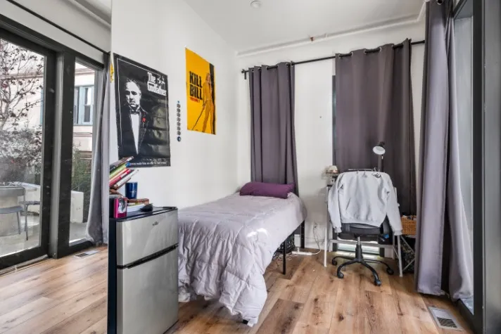 Cozy bedroom with wooden flooring, modern decor, and a large window bringing in natural light, creating a warm and inviting atmosphere.