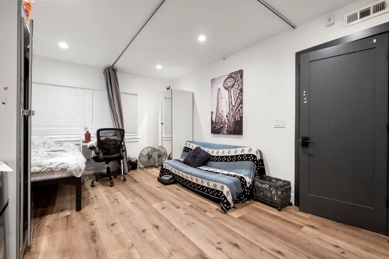 Bright and modern studio apartment with wooden flooring, cozy bed, stylish seating area, and chic black door.
