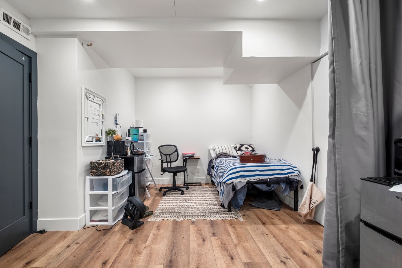Modern bedroom and workspace with stylish decor, featuring a cozy bed, wooden flooring, and ample storage solutions.