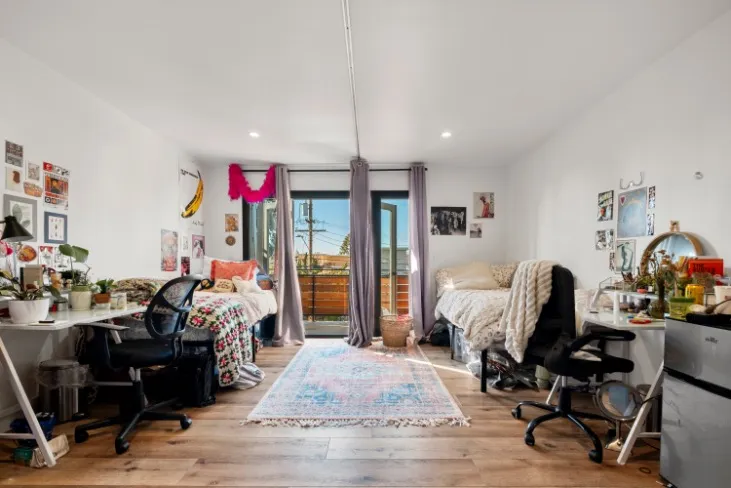 Bright and inviting double bedroom apartment with wooden flooring, vibrant decor, and ample natural light from a glass door leading to a balcony.