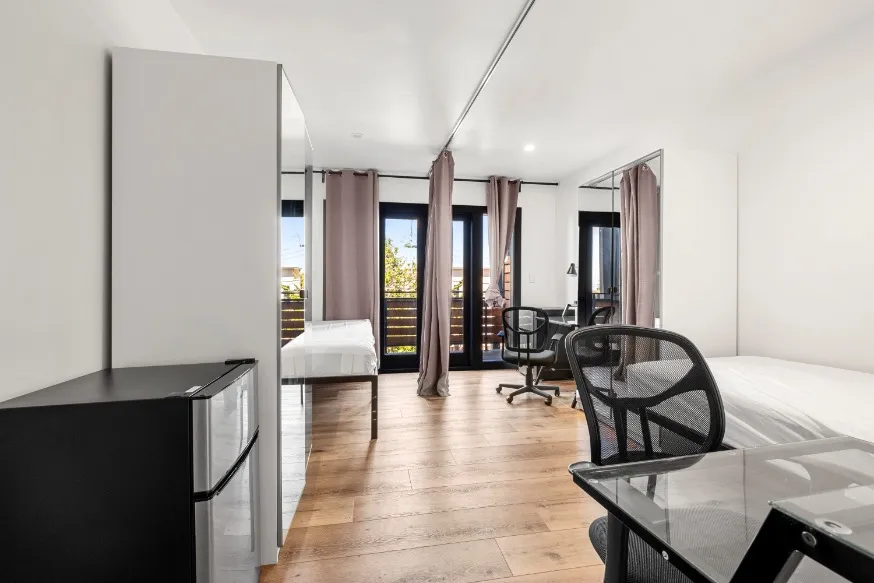Bright, modern bedroom with sleek furnishings, featuring a large window, hardwood floors, and a cozy workspace.