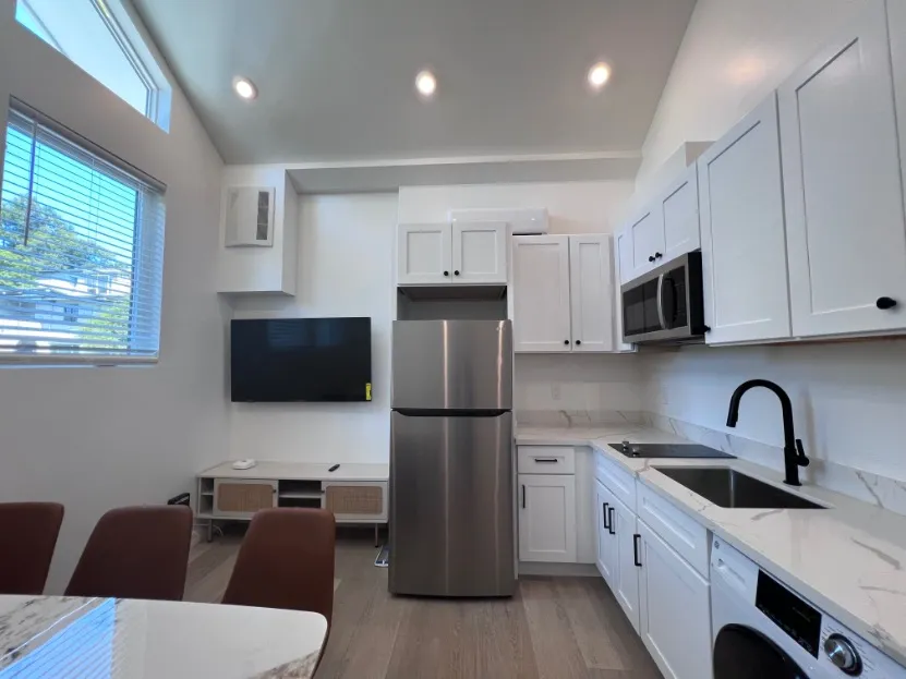 Modern kitchen and living area featuring sleek stainless steel appliances, elegant white cabinetry, and large windows providing abundant natural light.