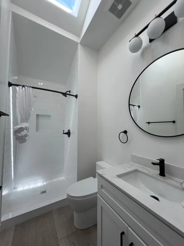 Bright and modern bathroom featuring a skylight, sleek shower, and elegant vanity with a stylish round mirror.
