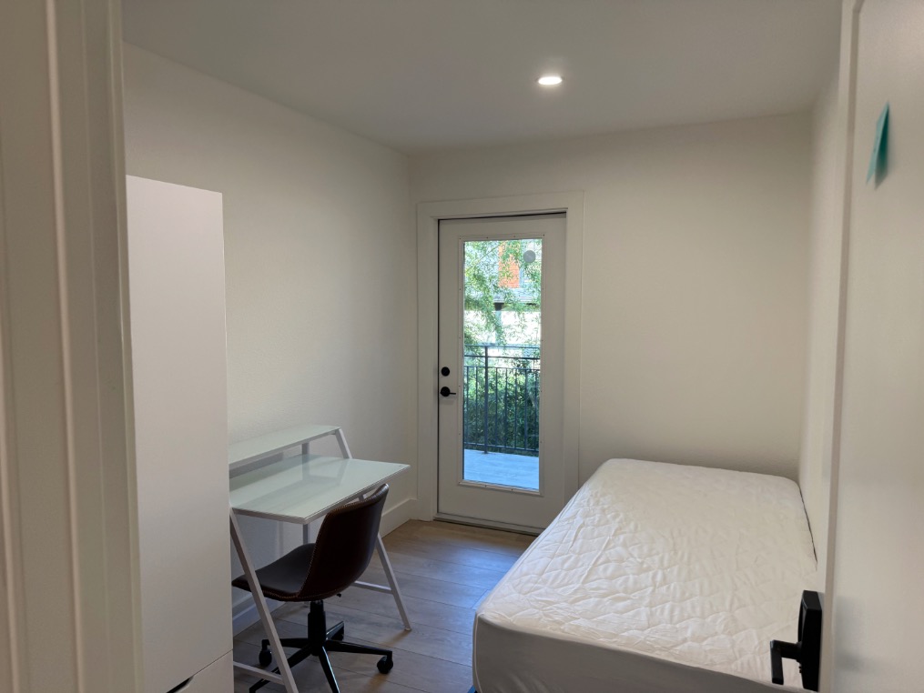 Bright single bedroom with minimalist design, featuring a bed, study desk, and private balcony access.