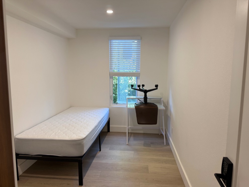 Bright and cozy room with a single bed and window offering natural light, featuring sleek hardwood floors and a modern minimalist design.