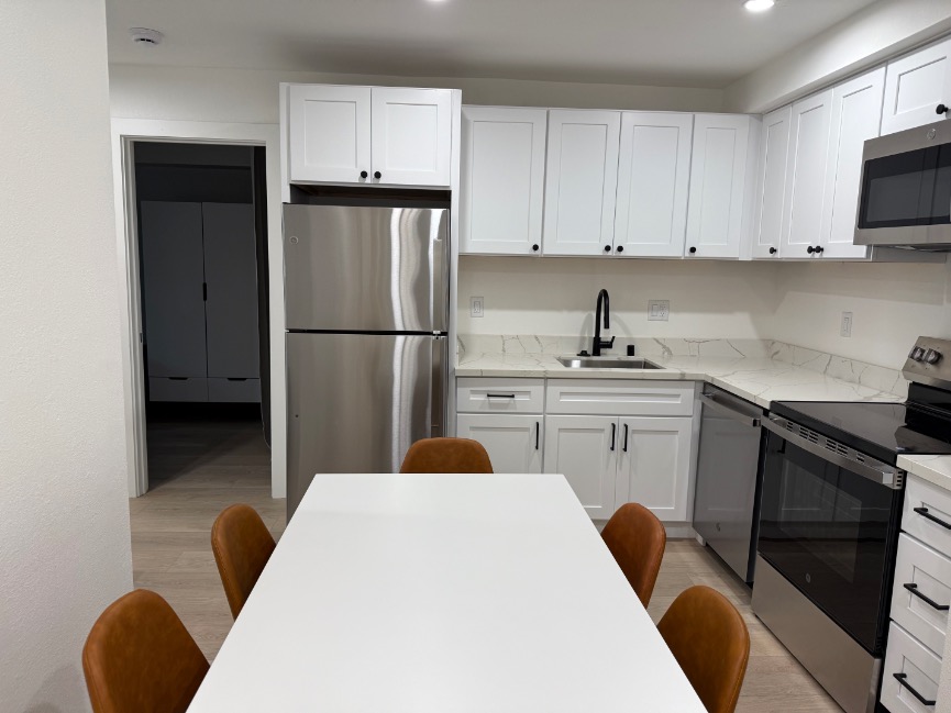 Modern kitchen with sleek white cabinets, stainless steel appliances, and a chic dining area.