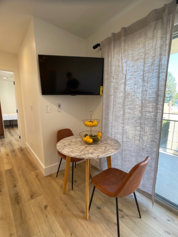 Cozy dining nook with a marble-top table, elegant leather chairs, and a wall-mounted TV, bathed in natural light.