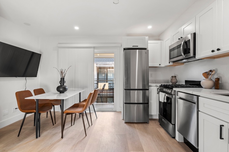 Modern kitchen and dining area with sleek white cabinets, stainless steel appliances, and a balcony view.