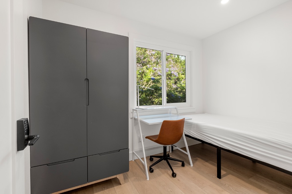 Bright and modern bedroom featuring a sleek wardrobe, cozy study area, and a window with a scenic view.