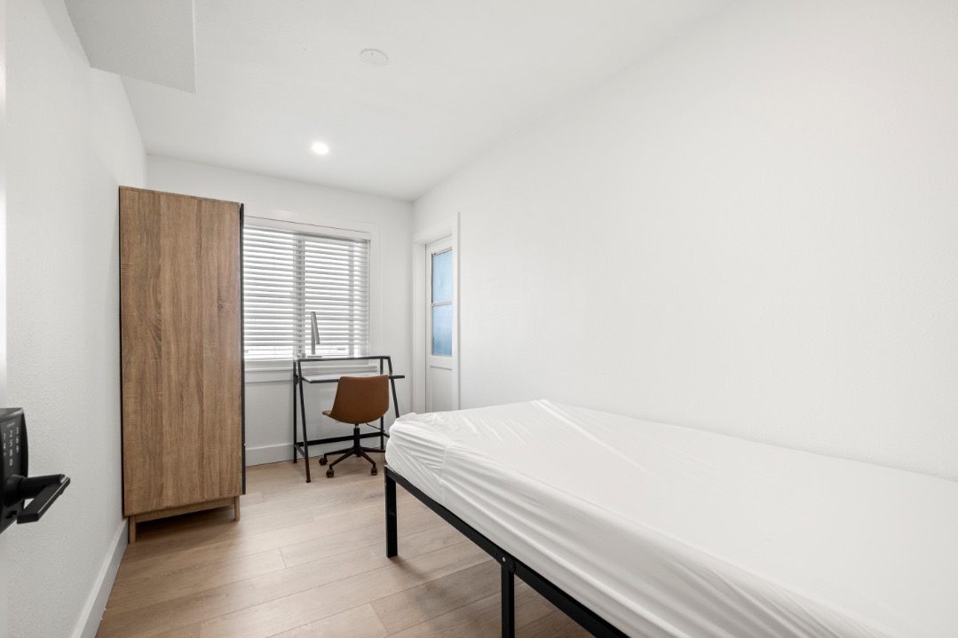 Cozy minimalist bedroom featuring a single bed, wooden wardrobe, and desk with a modern chair.