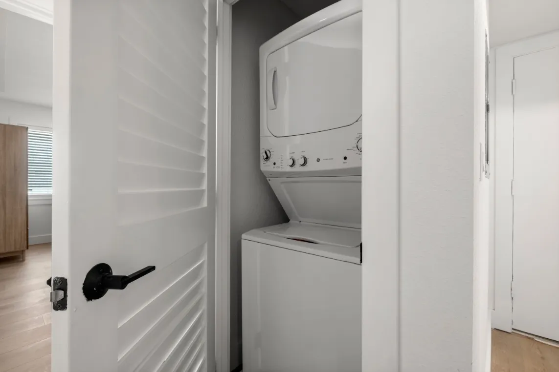 Compact laundry nook featuring a modern stacked washer and dryer set behind a white door.