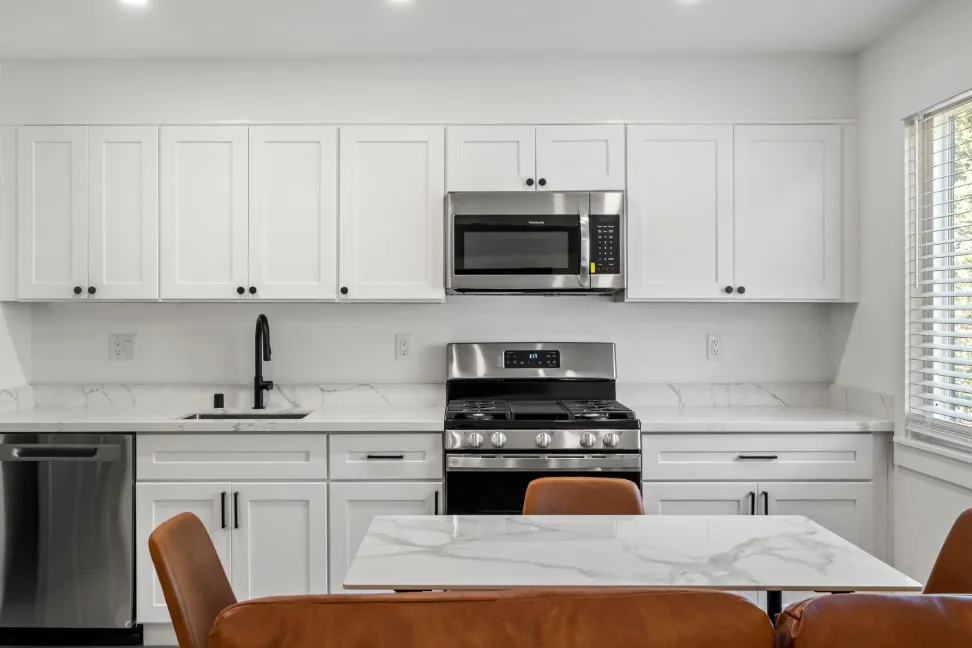 Modern kitchen featuring sleek white cabinets, stainless steel appliances, and a marble countertop dining area.
