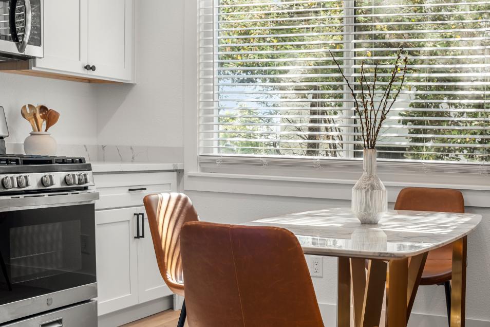 Bright and modern kitchen with sleek white cabinetry, stainless steel appliances, and stylish dining area overlooking sunny garden view.