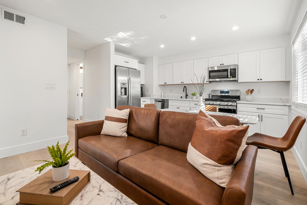 Bright and modern open-plan living area with a cozy leather sofa and sleek kitchen featuring stainless steel appliances and white cabinetry.