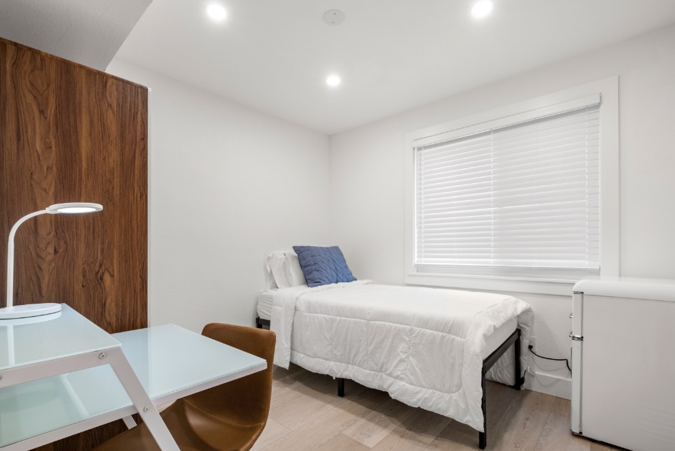 Modern, cozy bedroom featuring a single bed, white linens, and a sleek work desk with ambient lighting.