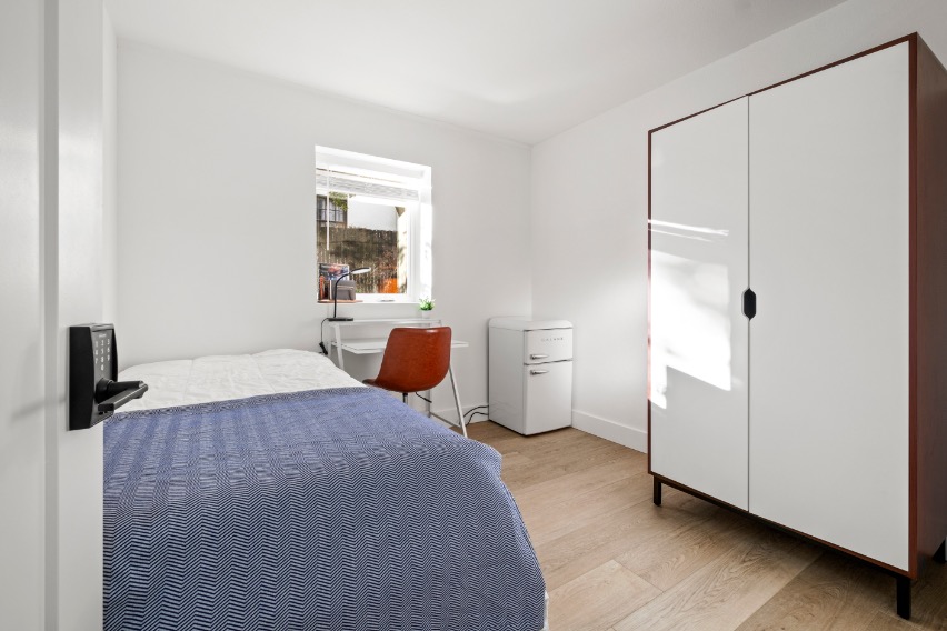 Bright and cozy bedroom with a modern white wardrobe, wooden floor, and natural light streaming through the window.