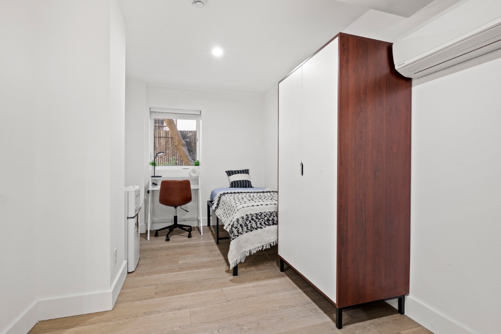 Modern bedroom with sleek wooden wardrobe, cozy bed, and compact study desk, accentuating minimalist style and functionality.