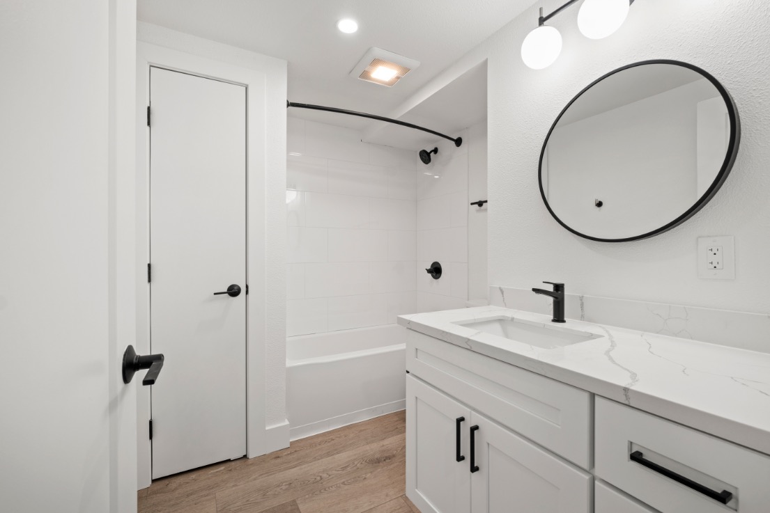 Sleek and modern bathroom with elegant fixtures, white vanity, and a stylish round mirror enhancing a minimalist design.